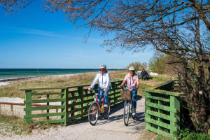 två cyklister cyklar över bro vid strand.