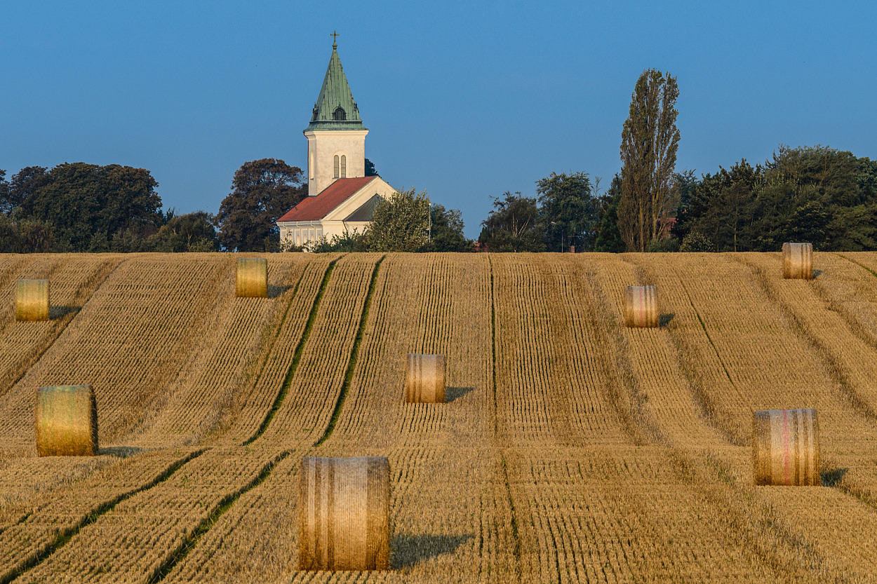 Fält med halmbalar framför kyrka.
