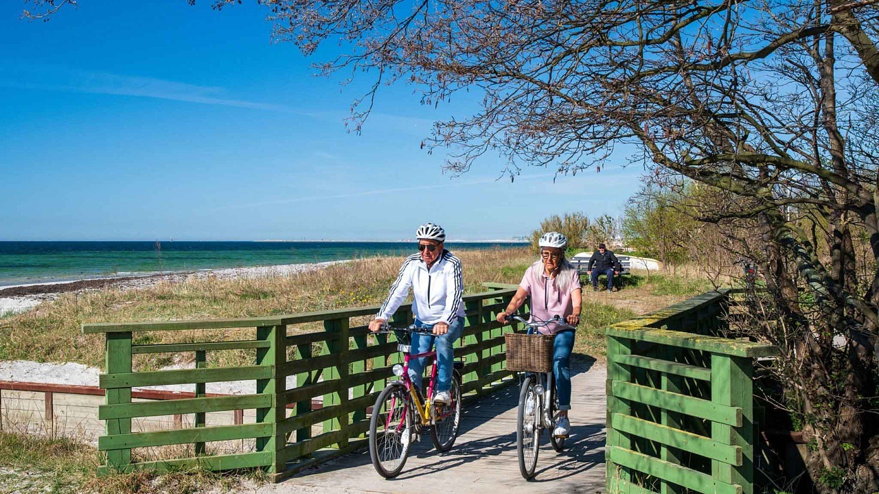 två cyklister cyklar över bro vid strand.