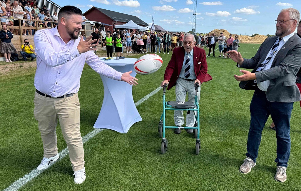 två män som kastar en rugbyboll framför publik