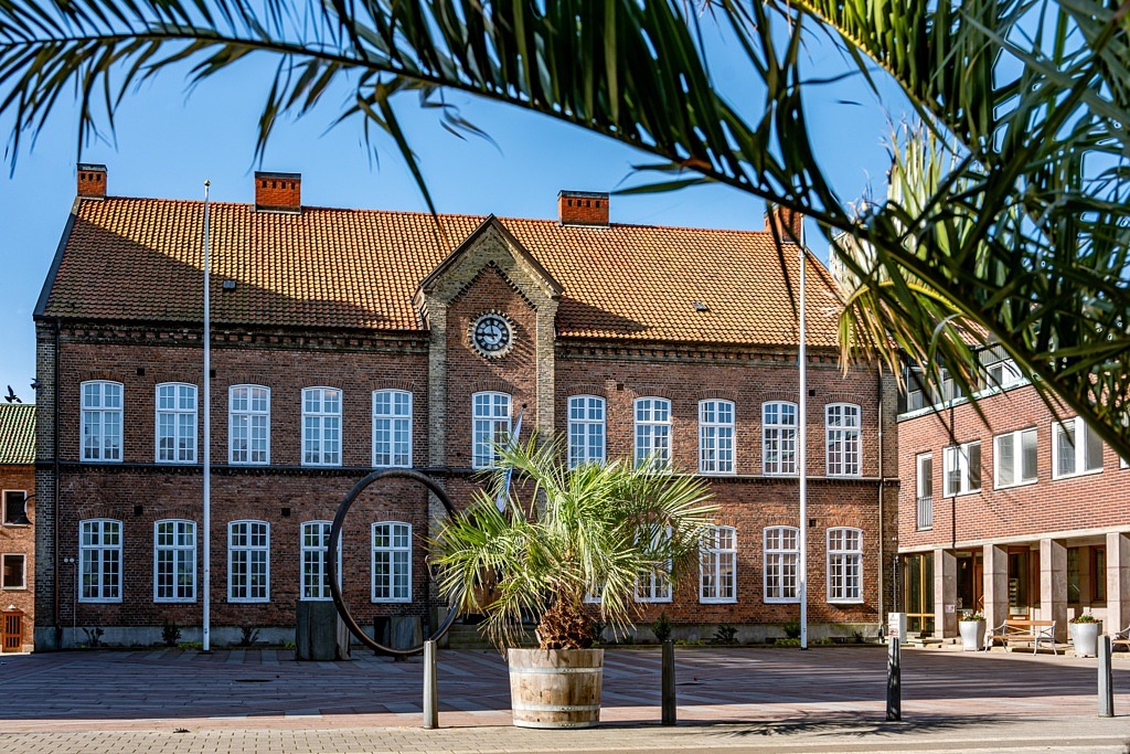 Byggnad i solsken med palm placerad på torget.