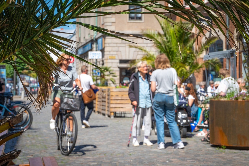 Gatumiljö, personer står och pratar med varandra och en cyklist cyklar förbi.