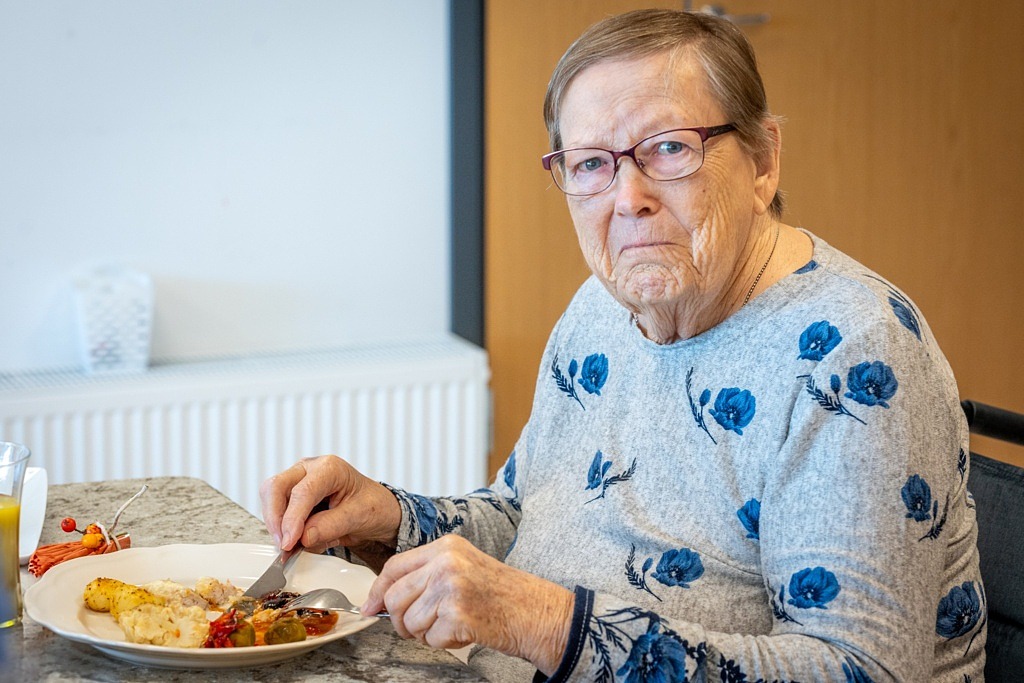 Kvinna i glasögon sitter vid matbordet och tittar in i kameran.