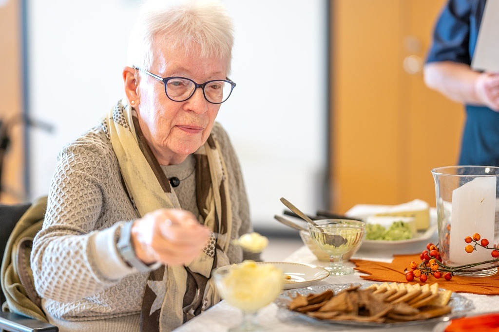 Kvinna med glasögon serverar sig själv vid ett bord med ostbricka.