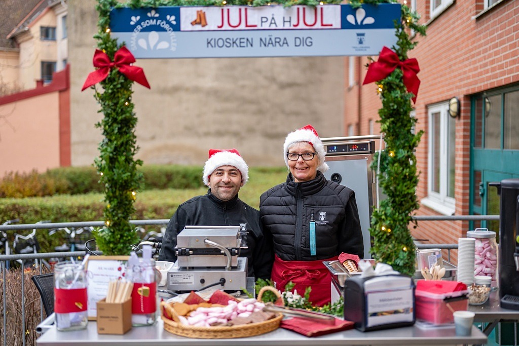 Två personer med tomteluvor står bakom ett uppdukat bord.